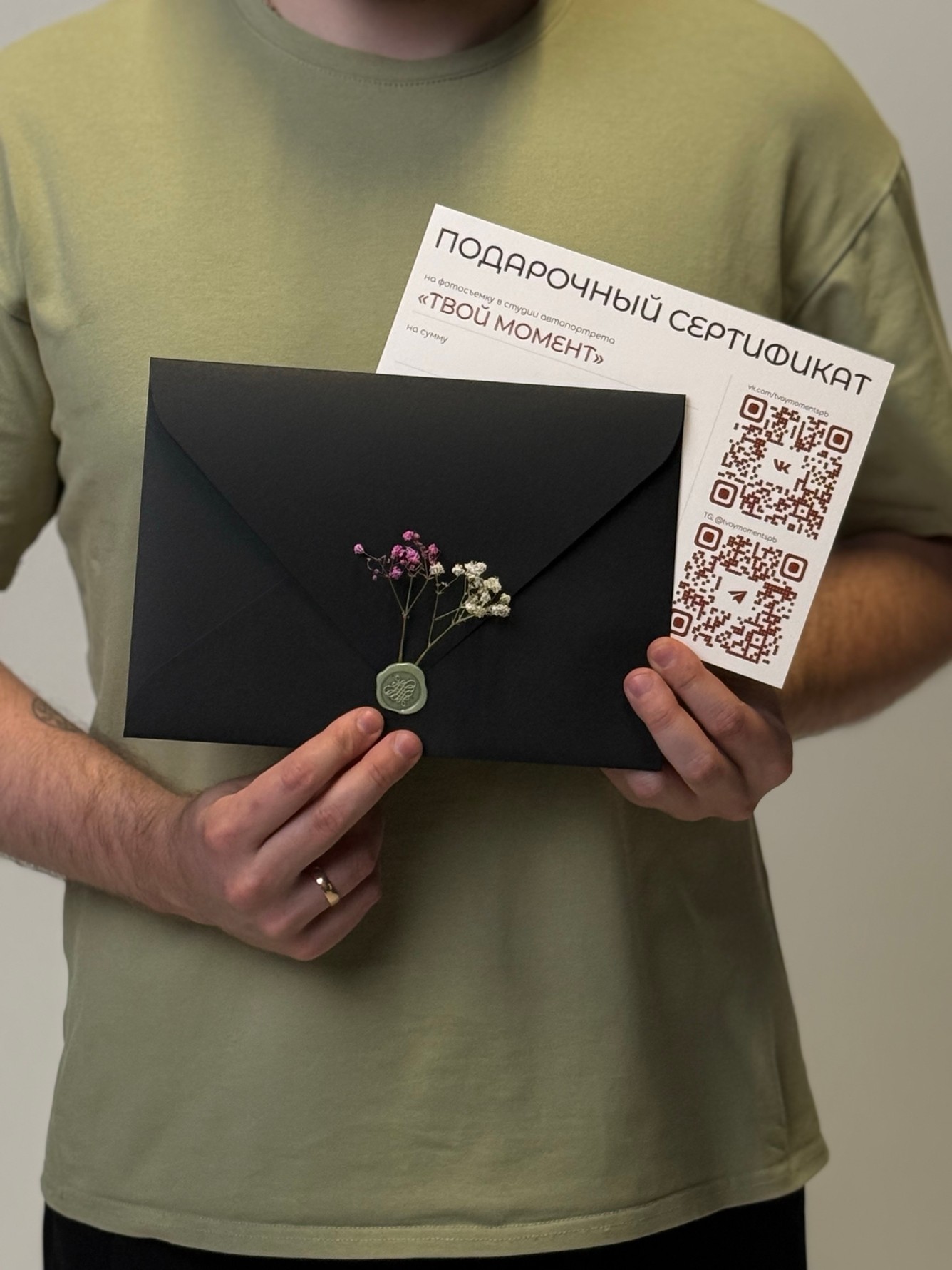 Подарочный сертификат «Твой момент» и черный конверт с сухоцветами в руках Подарочный сертификат «Твой момент» и черный конверт с сухоцветами в руках